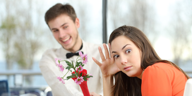 Disgusted woman rejecting a geek boy offering flowers in a blind date in a coffee shop interior