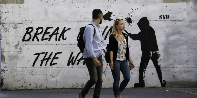 A couple walk in front of a wall with graffiti, near the UN buffer zone, "Green Line" that divide the Greek and Turkish Cypriot controlled areas in divided capital Nicosia in this eastern Mediterranean island of Cyprus, Friday, Nov. 11, 2016. The rival leaders of ethnically divided Cyprus are locked in crucial talks in Mont Pelerin, Switzerland that will determine whether a peace deal is within reach. (AP Photo/Petros Karadjias)