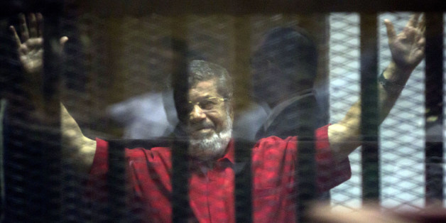 Former Egyptian President Mohammed Morsi, wearing a red jumpsuit that designates he has been sentenced to death, raises his hands inside a defendants cage in a makeshift courtroom at the national police academy, in an eastern suburb of Cairo, Egypt, Saturday, June 18, 2016. An Egyptian court has sentenced six people, including two Al-Jazeera employees, to death for allegedly passing documents related to national security to Qatar and the Doha-based TV network during the rule of Islamist president Mohammed Morsi. Morsi, the case's top defendant, was also sentenced on Saturday to 25 years in prison. He was ousted by the military in July 2013, and has already been sentenced to death in other cases. (AP Photo/Amr Nabil)