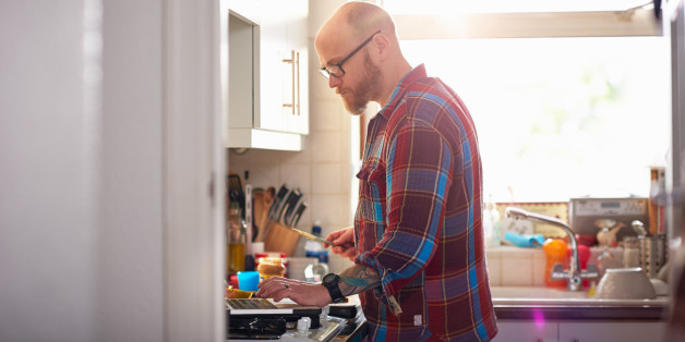 Man in kitchen using laptop whilst making lunch