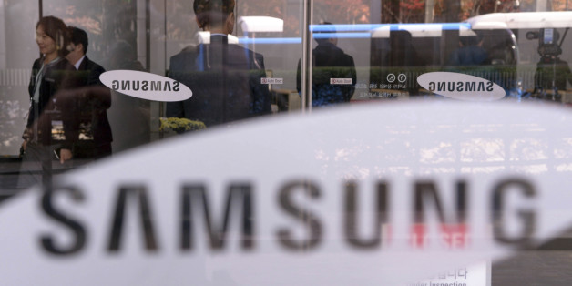 Employees walk past logos of Samsung Group at its headquarters in Seoul, South Korea, Wednesday, Nov. 23, 2016. South Korean prosecutors investigating a corruption scandal surrounding the country's president and her friend raided on Wednesday a unit of the country's largest business group, Samsung, and the national pension fund, as public outrage grows over Samsung's alleged link with the scandal. (Jang Se-young/Newsis via AP)