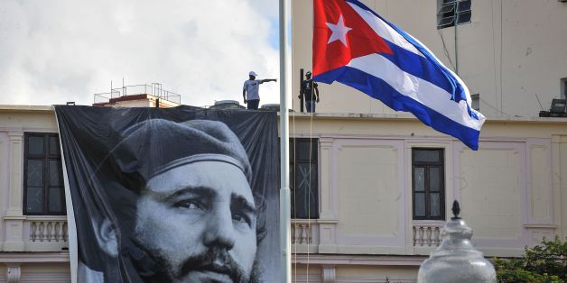 A Cuban flag flutters at half mast near a banner depicting Cuban revolutionary leader Fidel Castro, two days after his death, in Havana on November 27, 2016.Cuban revolutionary icon Fidel Castro died late November 25 in Havana, his brother, President Raul Castro, announced on national television. Castro's ashes will be buried in the historic southeastern city of Santiago on December 4 after a four-day procession through the country. / AFP / Yamil LAGE (Photo credit should read YAMIL LAGE/