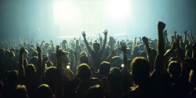 A general view of a rock concert taken from the back fo a venue showing the audience in silhouette raising their arms and cheering with bright lights shining from the stage, circa 1980. (Photo by Fin Costello/Redferns)