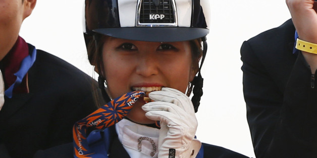 (L-R) South Korea's Kim Kyun-sub, Hwang Young-shik, Chung Yoo-yeon and Kim Dong-seon bite their gold medals as they pose after winning the equestrian Dressage Team competition at the Dream Park Equestrian Venue during the 17th Asian Games in Incheon September 20, 2014. REUTERS/Kim Hong-Ji (SOUTH KOREA - Tags: SPORT EQUESTRIANISM)
