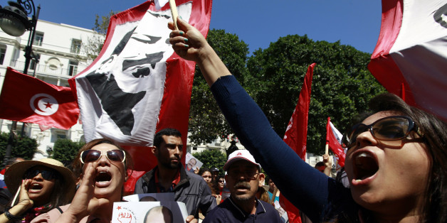A demonstrator (L) holds a portrait of the late Tunisian opposition leader Chokri Belaid as others wave flags and a poster of slain opposition leader Mohamed Brahmi at an event commemorating the Feast of the Martyrs at Avenue Habib Bourguiba in Tunis, April 9, 2014. REUTERS/Anis Mili (TUNISIA - Tags: CIVIL UNREST POLITICS ANNIVERSARY)