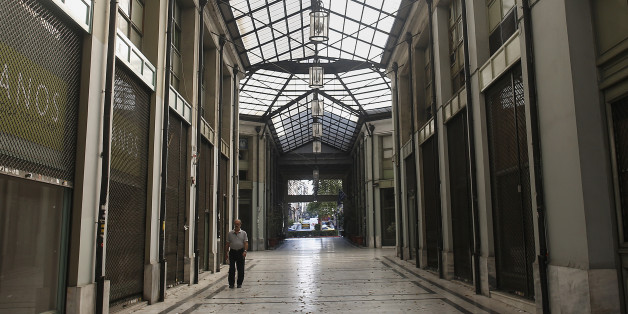 A pedestrian walks past closed and shuttered shops inside a shopping arcade in Athens, Greece, on Sunday, July 12, 2015. European finance chiefs said they were unlikely to strike a deal on the outlines of a third Greek bailout, threatening to delay the cash infusion Prime Minister Alexis Tsipras desperately needs. Photographer: Simon Dawson/Bloomberg via Getty Images