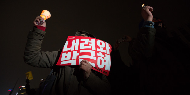 A protester holds a candle and a placard during a rally in Seoul, South Korea, on Saturday, Nov. 26, 2016. Hundreds of thousands of South Korean protesters marched to President Park Geun-hye's office, beating drums and chanting slogans, even as lawmakers considered impeaching her over an influence-peddling scandal. Photographer: SeongJoon Cho/Bloomberg via Getty Images