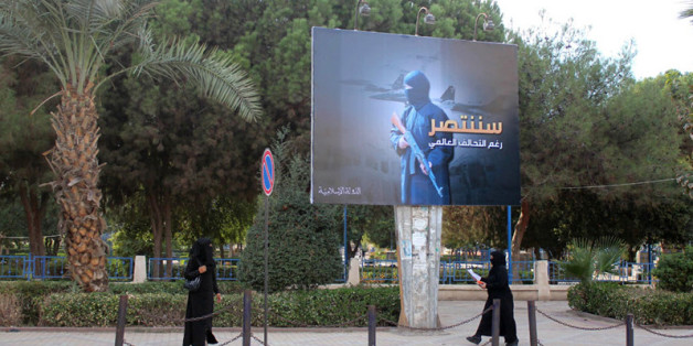 Des femmes en niqab marche sous un panneau érigé par le groupe de l'Etat islamique (Daech) dans le cadre d'une campagne de l'EI contrôlant la ville syrienne de Raqqa, le 1er novembre 2014. En arabe sur le panneau, il est écrit : "Nous devons être triomphant, malgré la coalition mondiale"