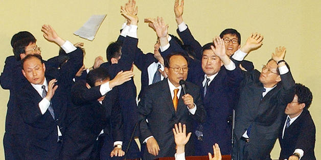 SEOUL, REPUBLIC OF KOREA: South Korea's parliamentary security guards surround Speaker Park Kwan-Yong (C) as he announces the National Assembly's vote results of 193 votes to two to impeach President Roh Moo-Hyun, in Seoul 12 March 2004. Roh was suspended from office after opposition lawmakers passed an historic impeachment vote, leaving the country in political chaos. AFP PHOTO (Photo credit should read STR/AFP/Getty Images)