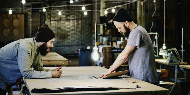 Two leatherworkers discussing product design at table in leather workshop