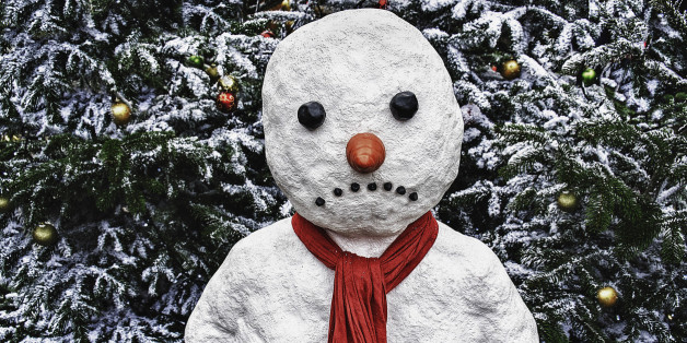 A snowman stands in front of a Xmas tree with a sad expression.
