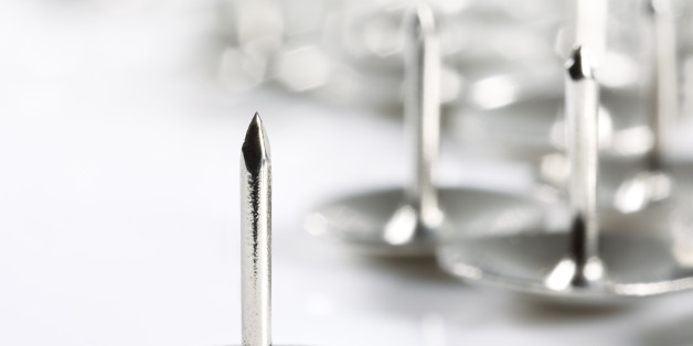Close up image of a single chrome thumb tack pointing menacingly up in the air with others in soft focus grouped in the background