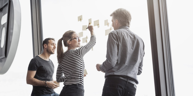 Business colleagues discussing over notes stuck to glass window in office