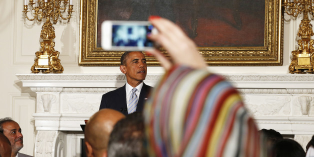 A Muslim woman takes a photo as U.S. President Barack Obama speaks while hosting an Iftar dinner at the White House in Washington July 14, 2014. Iftar is the meal after sunset that breaks the day of fasting during Ramadan. REUTERS/Kevin Lamarque (UNITED STATES - Tags: POLITICS RELIGION)