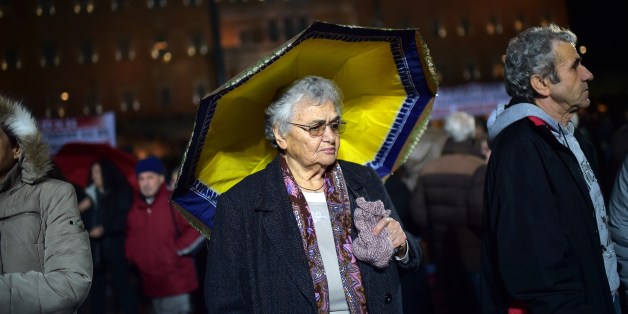 An elderly woman stands under a yellow umbrella outside the parliament in Athens on February 27, 2015 as supporters of the Communist Party of Greek (KKE) gather for an anti-government demonstration. AFP PHOTO / ARIS MESSINIS (Photo credit should read ARIS MESSINIS/AFP/Getty Images)