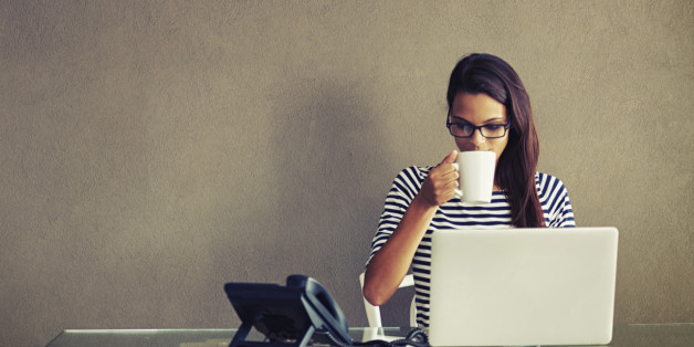 An attractive young businesswoman having coffee while working at her office desk