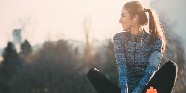 Young beautiful woman resting after the jogging in the city.She is listening to the music.