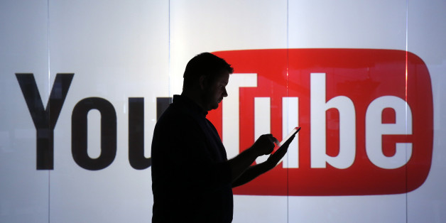 A man is seen as a silhouette as he checks a mobile device whilst standing against an illuminated wall bearing YouTube Inc.'s logo in this arranged photograph in London, U.K., on Tuesday, Jan. 5, 2016. YouTube Inc. provides consumer media and entertainment through its website. Photographer: Chris Ratcliffe/Bloomberg via Getty Images