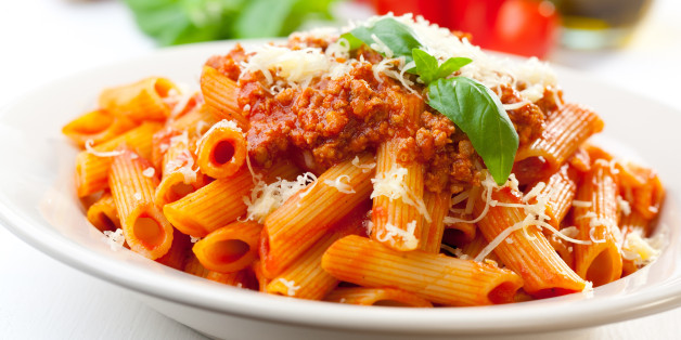 Plate of penne bolognese with ingredients in the background.
