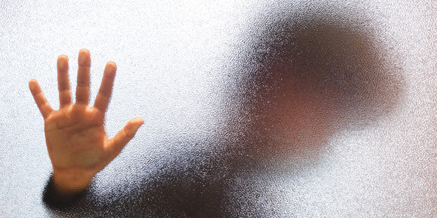 Blurred sad boy leaning open hand against glass door.