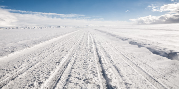 A snow covered road leads through an empty winter landscape under clear sky. Near Garrison, Utah.