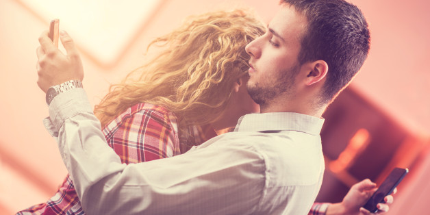 Young couple embracing and each of them text messaging on their own smart phone.
