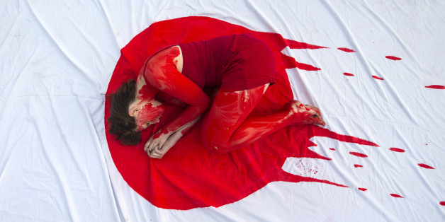 An Israeli member of the 'Taiji Dolphin Action Group', with a red body painting to evok blood, is curled up on a sheet depicting the Japanese flag, during a protest against the killing of dolphins, notably in the Japanese city of Taiji on January 30, 2014 outside the building housing the Japanese Embassy, in the Mediterranean coastal city of Tel Aviv. Similar rallies outside Japanese consulates and embassies were expected to take place worldwide. AFP PHOTO / JACK GUEZ (Photo credit should