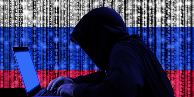 Hacker in a dark hoody sitting in front of a notebook with digital russian flag and binary streams background cybersecurity concept