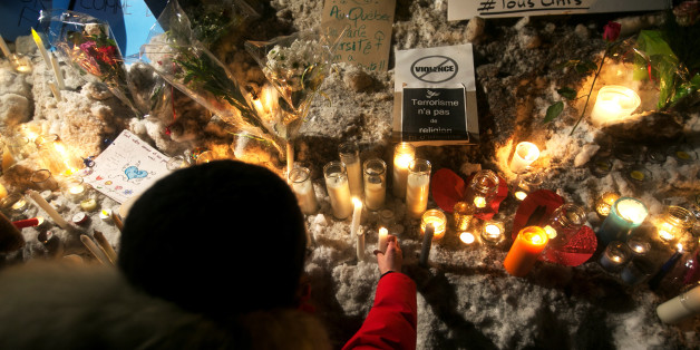 A woman places a candle at a memorial site near a sign saying "no violence" and "terrorism has no religion or identity" following a vigil held in honour of the victims of a shooting in a Quebec mosque in Quebec City, Quebec January 30, 2017. REUTERS/Christinne Muschi