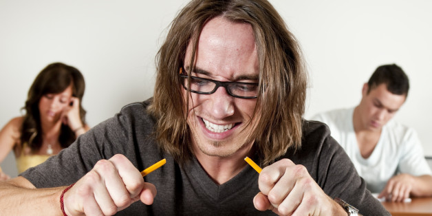 A young man in school is frustrated with his assignment and breaks a pencil in half.