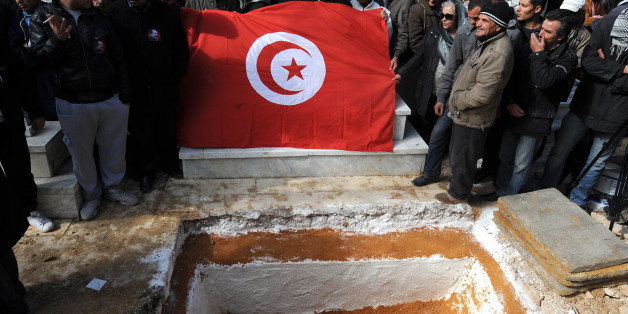 Mourners hold a Tunisian flag as they gather around the grave of assassinated opposition leader Chokri Belaid during his burial at El-Jellaz cemetery in a suburb of Tunis on February 8, 2013. Tunisian police fired tear gas and clashed with protesters as tens of thousands joined the funeral of Belaid whose murder plunged the country into new post-revolt turmoil. AFP PHOTO/FETHI BELAID (Photo credit should read FETHI BELAID/AFP/Getty Images)