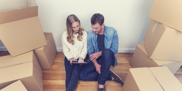 Young couple sitting in new house with packing boxes. They look like they have just moved in and they are very happy, smiling and talking. They are using a digital tablet, sitting on the floor in casual clothes. Copy space.