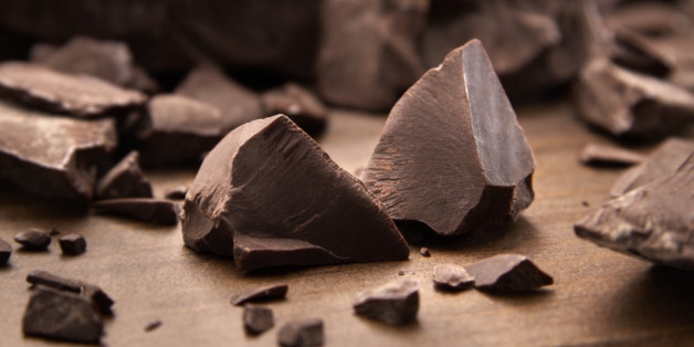 Pieces of dark chocolate spread out on a wooden background.