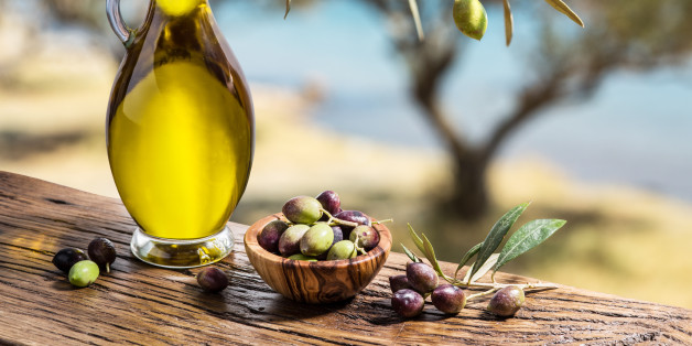 Olive oil and berries are on the wooden table under the olive tree.