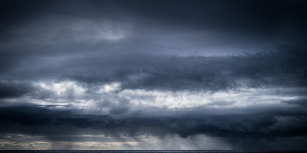 A squall forms over the Pacific Ocean, leaving the sky dark and stormy. In the distance rain falls on the horizon. Image is dark and cold. Hana, Maui.