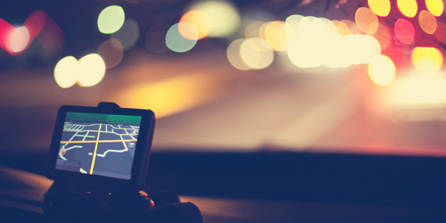 Night shot of GPS navigational system on dashboard of car. Traffic lights are visible through windshield.