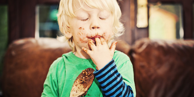 Little boy licking chocolate off his fingers and wooden spoon while making cakes.