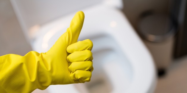 Close up of female hand with yellow protective rubber glove showing thumb up ok sign against clean toilet. Spring cleaning