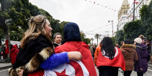 Two Tunisian women embrace as one wears the national flag, during a rally on January 14, 2017 in the Habib Bourguiba Avenue in the capital Tunis to mark the sixth anniversary of the 2011 revolution. / AFP / FETHI BELAID (Photo credit should read FETHI BELAID/AFP/Getty Images)