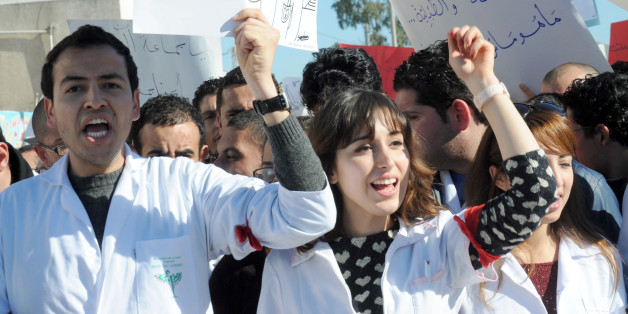 Tunisian doctors shoot anti-government slogans during a demonstration against a draft bill that aims at forcing them to work in rural areas on January 7, 2014 outside the headquarters of the National Constituent Assembly where debates take place on Tunisia's new constitution. (L) the placard reads words by late Nelson Mandela 'A decision taken without us but about us is a decision taken against us'. AFP PHOTO / FETHI BELAID (Photo credit should read FETHI BELAID/AFP/Getty Images)