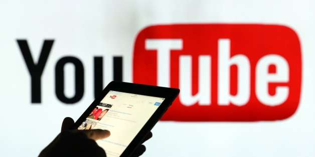 A man is seen as a silhouette as he checks a mobile device whilst standing against an illuminated wall bearing YouTube Inc.s logo in this arranged photograph in London, U.K., on Tuesday, Jan. 5, 2016. YouTube Inc. provides consumer media and entertainment through its website. Photographer: Chris Ratcliffe/Bloomberg via Getty Images