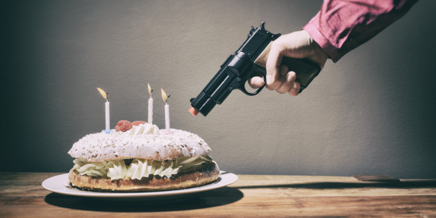 A woman threatens a delicious cream and raspberry birthday or anniversary cake with a toy gun at point blank range. Maybe something to do with weight loss or dietary problems; sugar, gluten, dairy or an unwelcome birthday or anniversary. Only the hand and arm of the woman is seen; the cake has three lit candles. Camera: 36MP Nikon D800E.