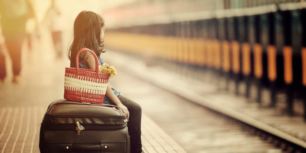 Little girl waiting in a railway station with bag and flower bouquet.