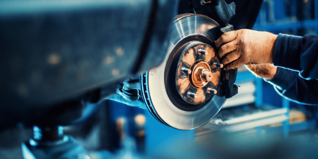 Closeup of unrecognizable mechanic replacing car brake pads. The car is lifted with hydraulic jack at eye level.