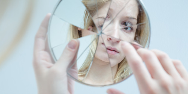 Insecure pretty young woman holding broken mirror
