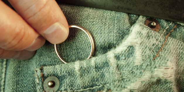 Closeup of a man?s hand put in or taking out a wedding ring in the worn jeans pocket. Concept of infidelity or asking in marriage.