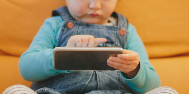 Mixed race 2 year old child sitting on a couch and playing with a smartphone