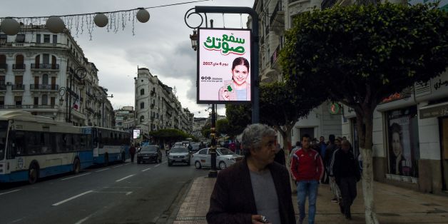 A picture taken on April 6, 2017 shows an illuminated billboard with the slogan 'make your voice heard' written in Arabic as pedestrians walk along a sidewalk in the Algerian capital Algiers.Campaigning starts on April 9, 2017 for Algeria's parliamentary polls in May, as authorities desperately try to persuade disillusioned voters that their opinion counts. Slogans reading 'make your voice heard' are found on on billboards and posters plastered in towns and villages across the North African coun