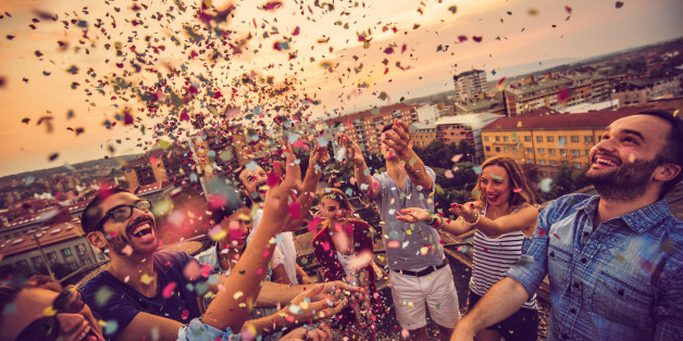 Couple of friends having a party on the rooftop of the building at sunset, dancing and trowing a confetti in the air - celebrating their youth and life