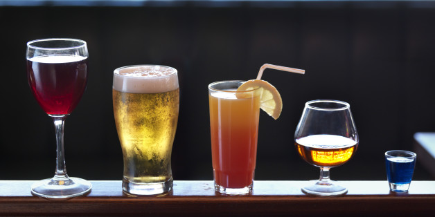 Standing on a banister, an assortment of various sizes and shapes of alcoholic drinks, ranging from shot, brandy, cocktail, beer and wine